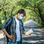 Male tourists stand and look at the map on the road.